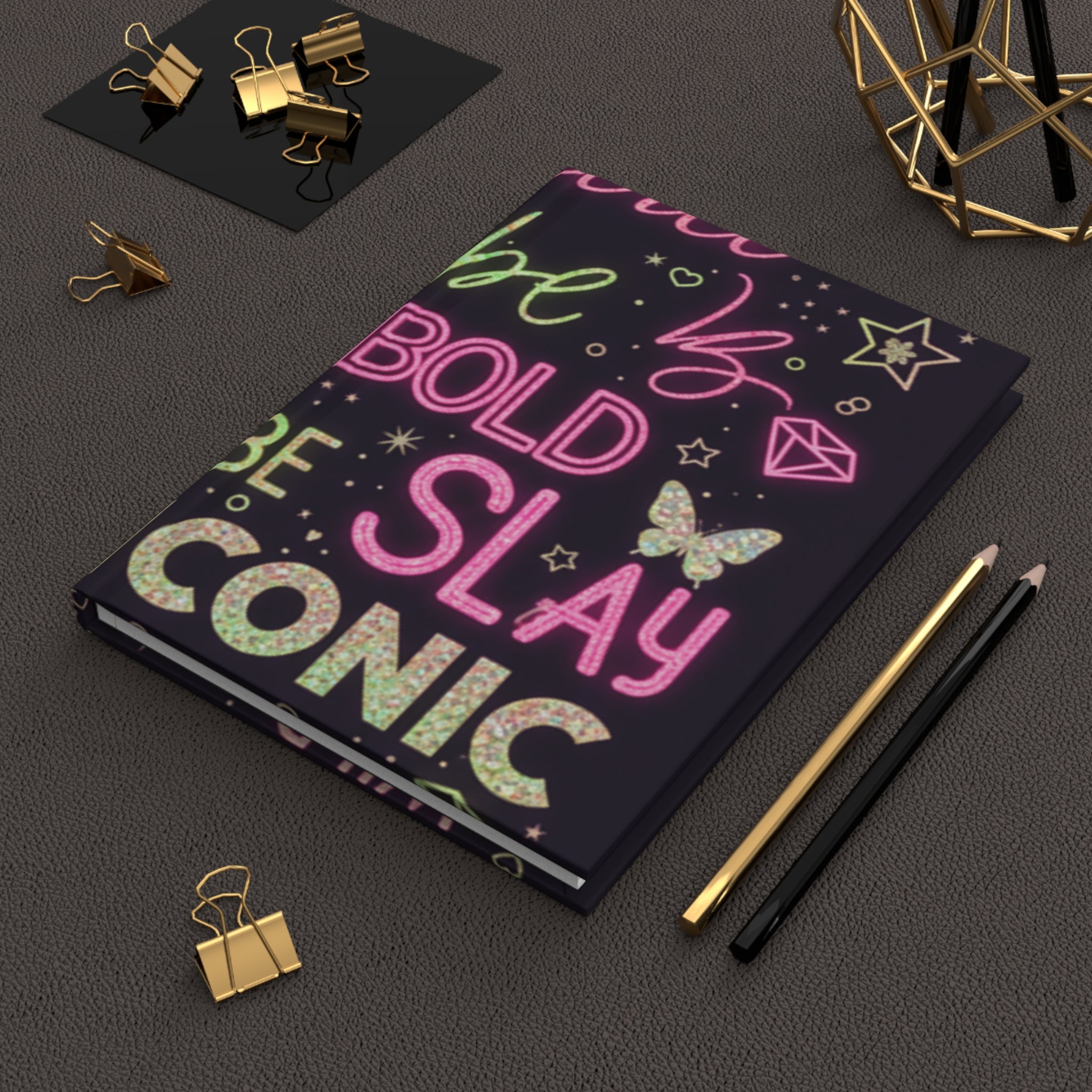 Diario rigido opaco con copertina scura e testo multicolore “SLAY” e “ICONIC”.